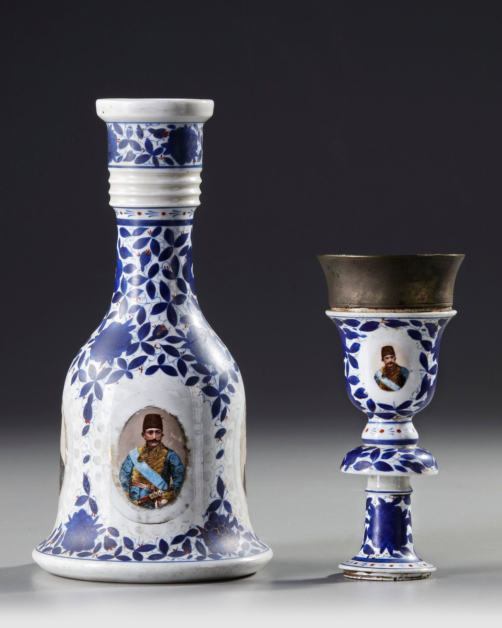 A QAJAR QALYAN SET, LATE 19TH-EARLY 20TH CENTURY: Porcelain Qalyan with blue floral motifs and portrait medallions of Naser al-Din Shah and Mozaffar al-Din Shah Qajar. Includes metal-topped stove. H. base: 26.5 cm; stove: 15 cm. Minor wear and oxidat