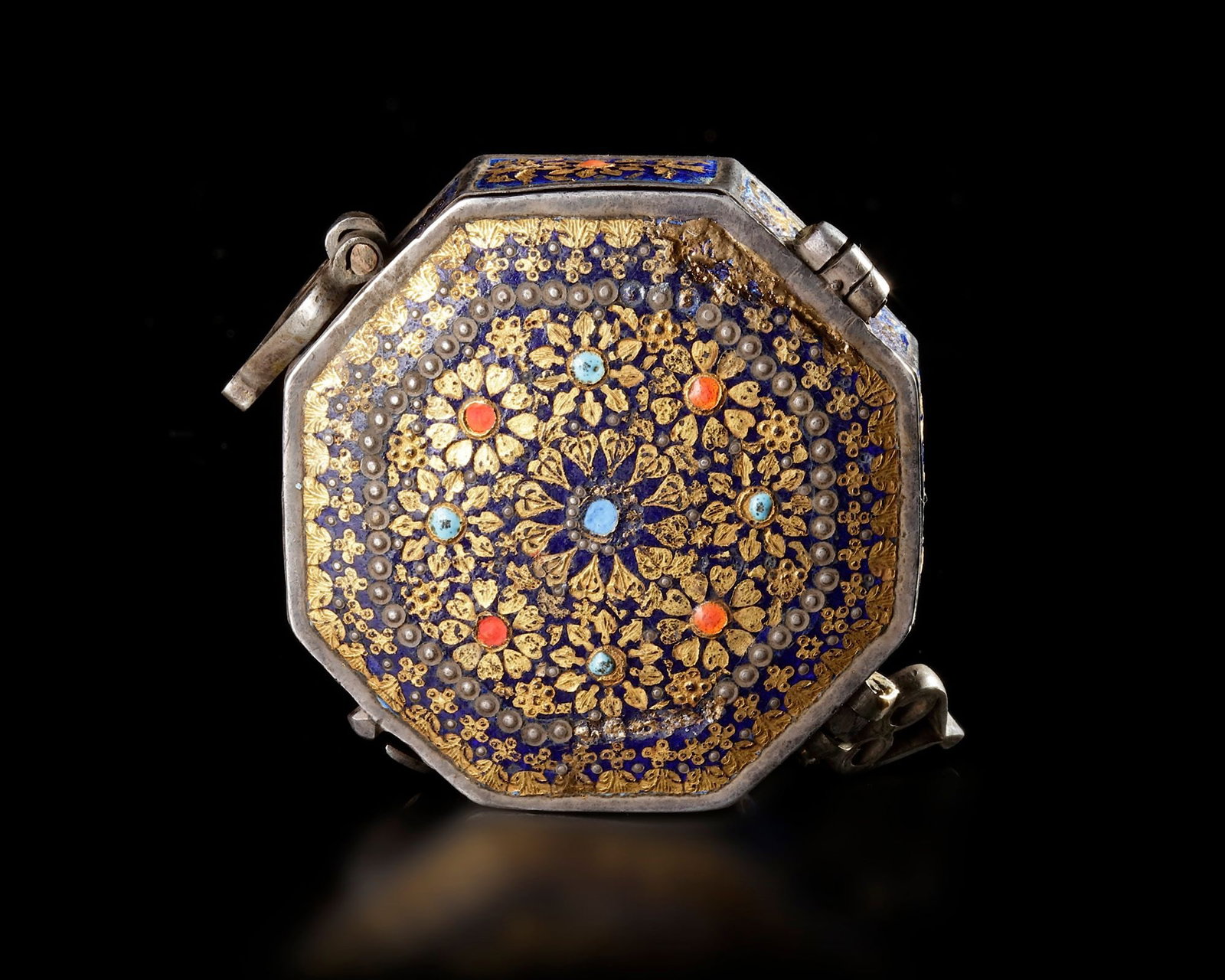 AN INDIAN ENAMELLED SILVER AMULET BOX, 19TH CENTURY: A finely crafted octagonal Indian silver box from the 19th century, richly decorated with colorful enamel. The lid displays an intricate floral rosette design in gold over deep blue enamel, accented w