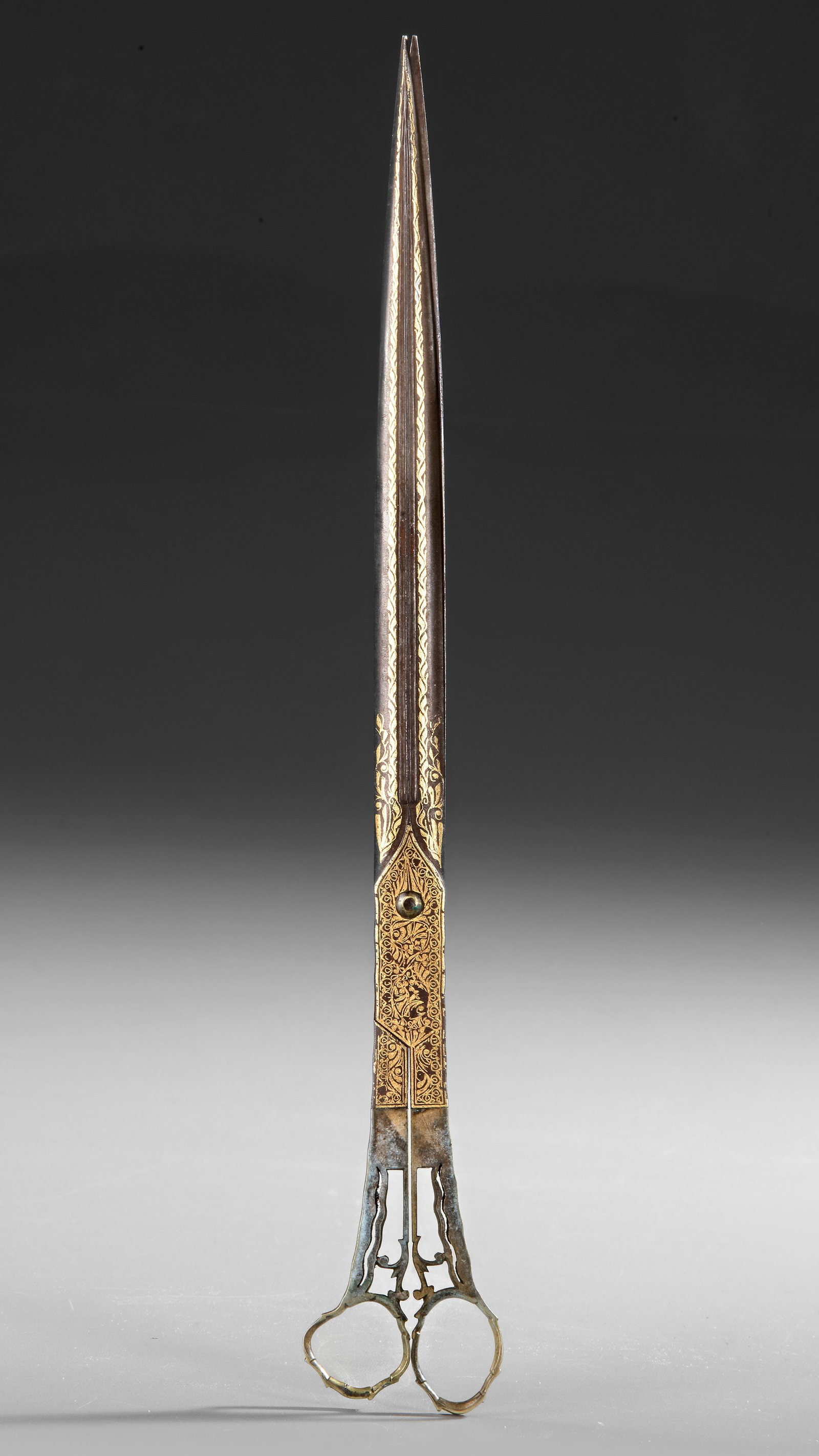 CALLIGRAPHERS SCISSORS, OTTOMAN TURKEY, 19TH CENTURY: Elegant Ottoman calligraphers scissors made of steel with double-gutted, gold-inlaid blades featuring plant motifs. Scalloped rings; some oxidation and rust present. Length: 27.8 cm.