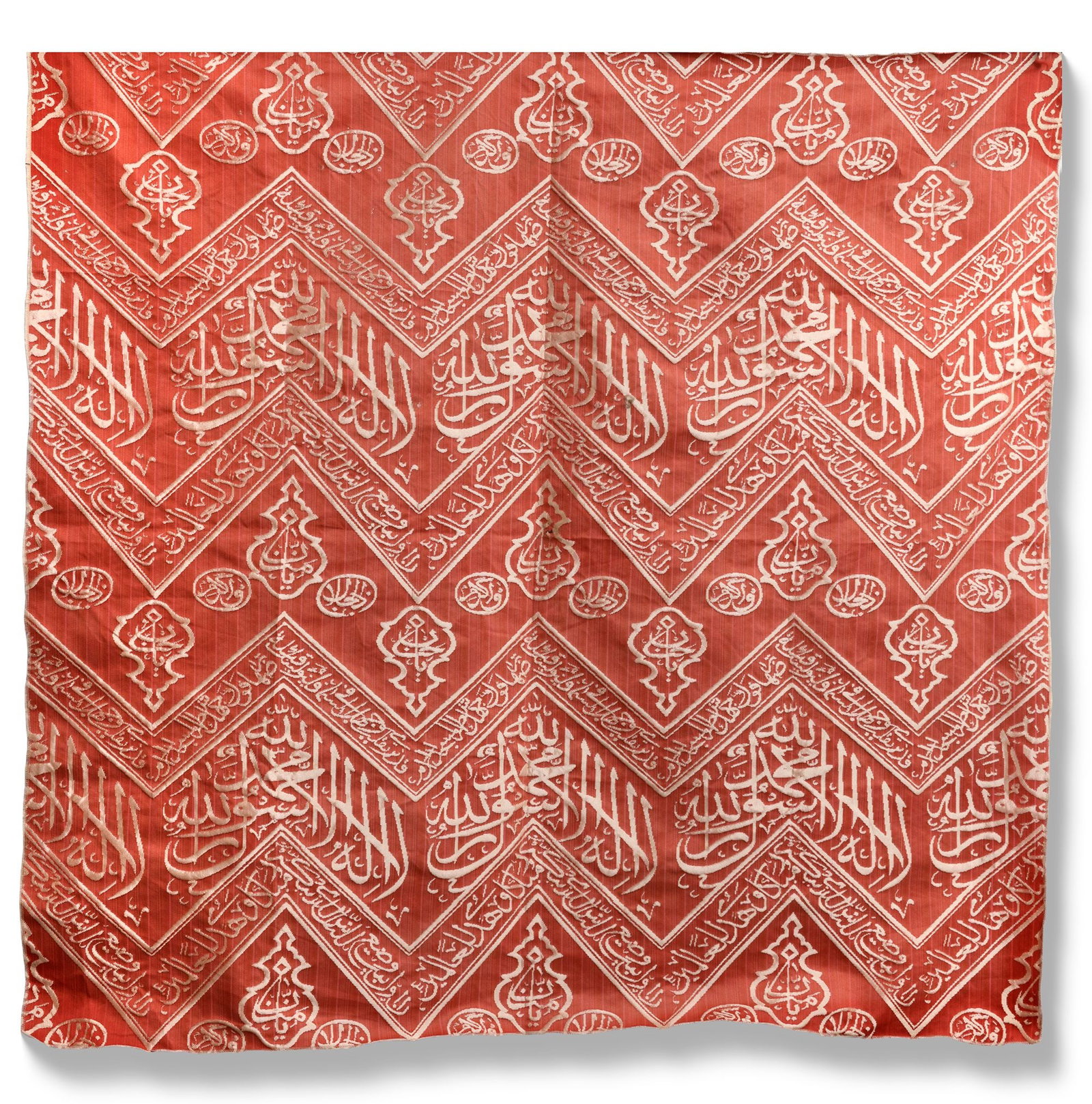 AN OTTOMAN RED EMBROIDERED SILK KISWA FRAGMENT, TURKEY OR EGYPT 20TH CENTURY: A fragment from the inner curtain of the sacred kiswa that lines the interior wall of the Kaaba, woven in cream-colored silk against a rich dark red background. The design features chevron patterns in