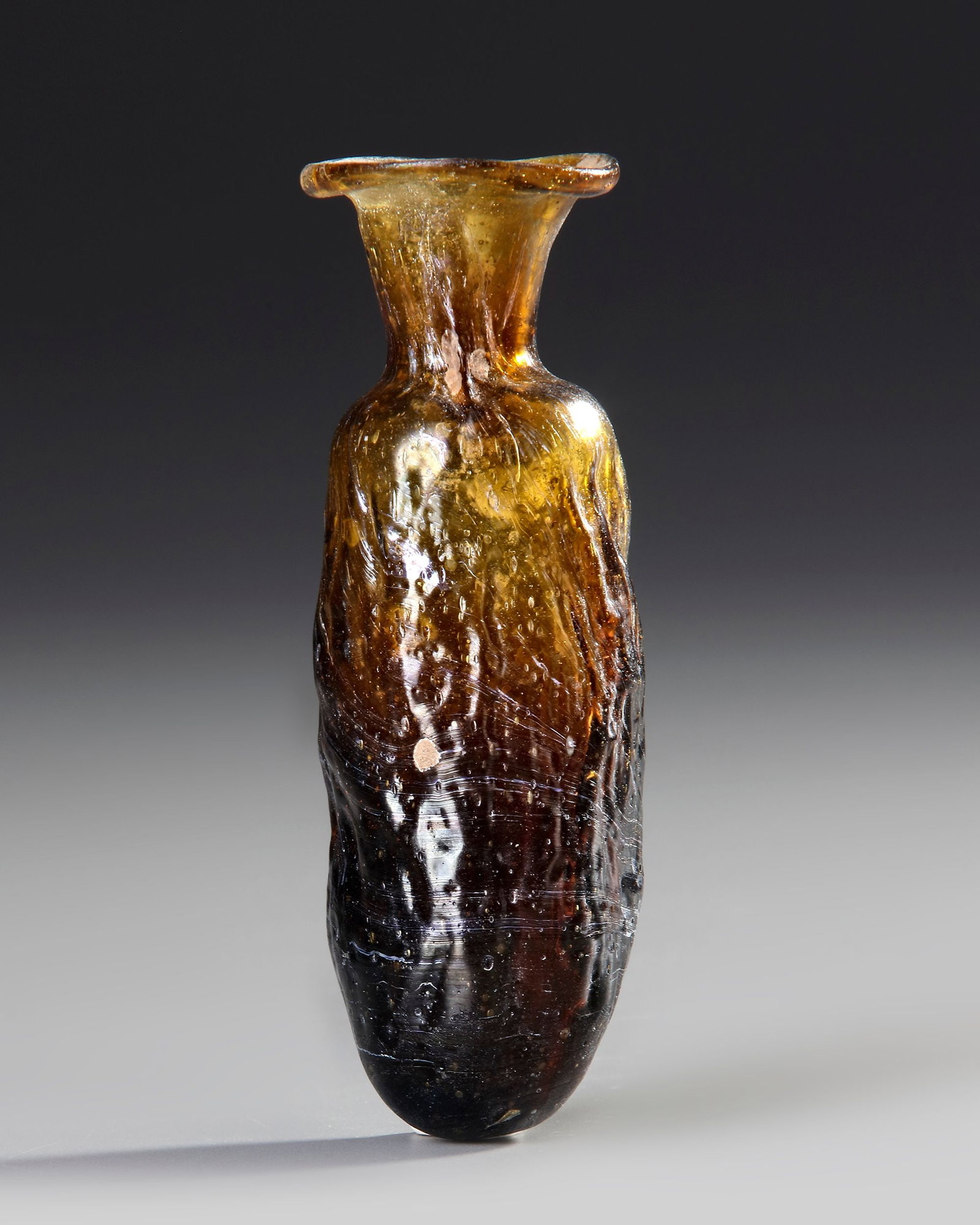 SIDONIAN MOLD-BLOWN EWER, VASE, 1ST CENTURY AD: Of elongated, slightly tapering form, the thick amber-brown glass rising to a narrow neck with a broad, out-turned rolled rim. The body is irregularly shaped and exhibits pronounced vertical and horiz