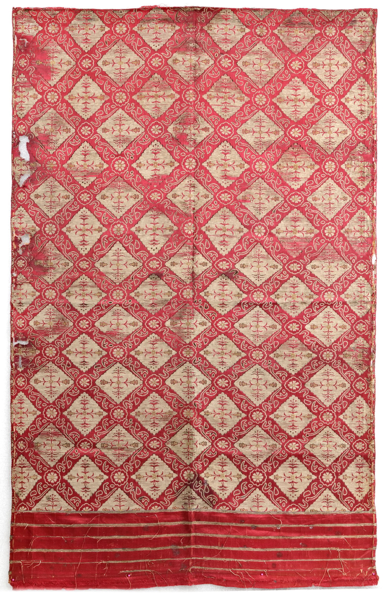 AN OTTOMAN SILK AND METAL-THREAD KEMHA FRAGMENT, BURSA TURKEY, 16TH-17TH CENTURY: Of rectangular shape, threads on a silk cream ground with black voided silk outlines on a red silk ground, depicting rows of diamond shapes enclosing flower heads and foliage. 95 by 68 cm.