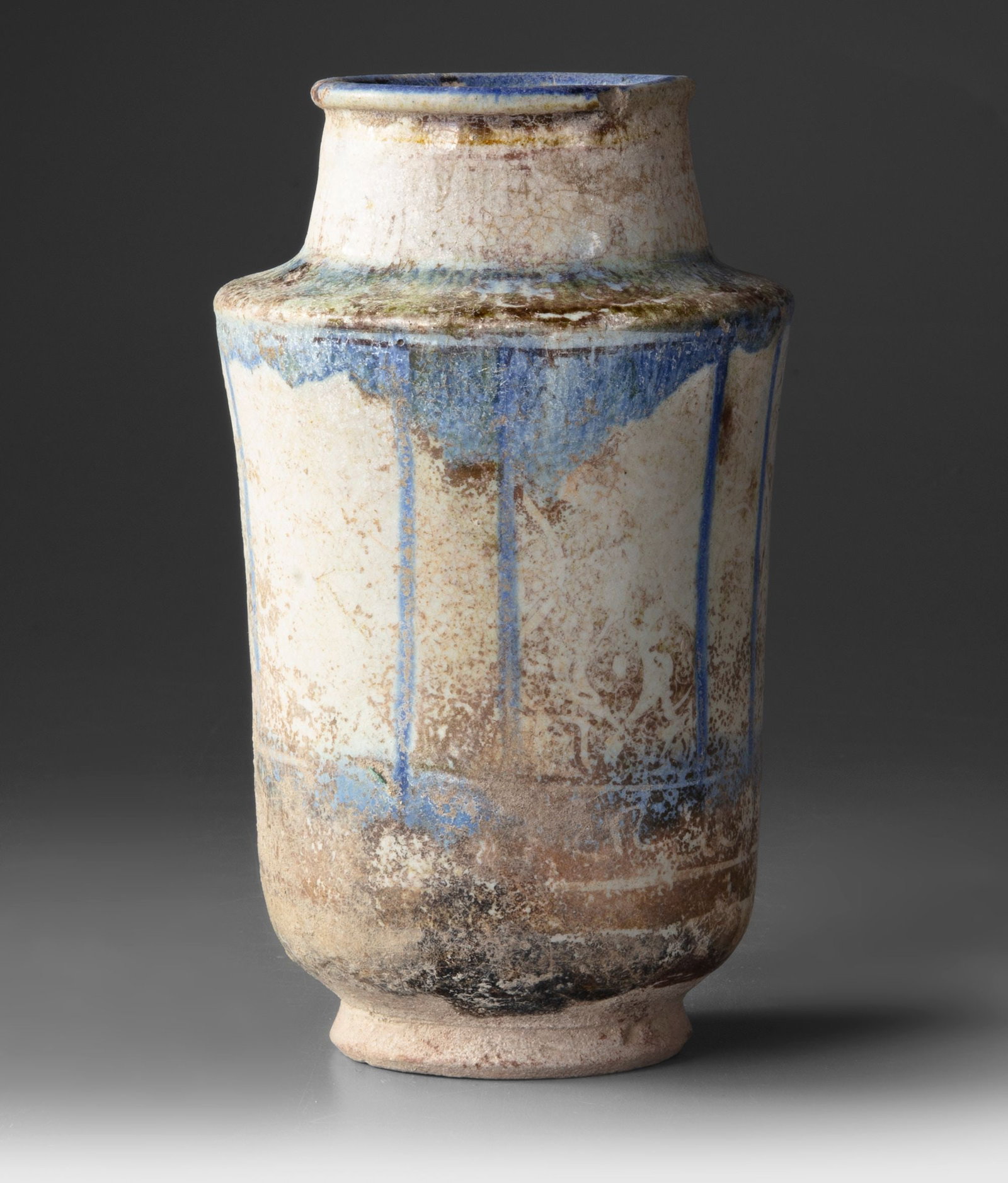 A KASHAN POTTERY ALBARELLO, PERSIA 13TH CENTURY: Of cylindrical form with a gently waisted body, short neck, and flared rim, the vessel is covered in a creamy white glaze painted in cobalt blue with vertical bands and a band at the shoulder. The fre