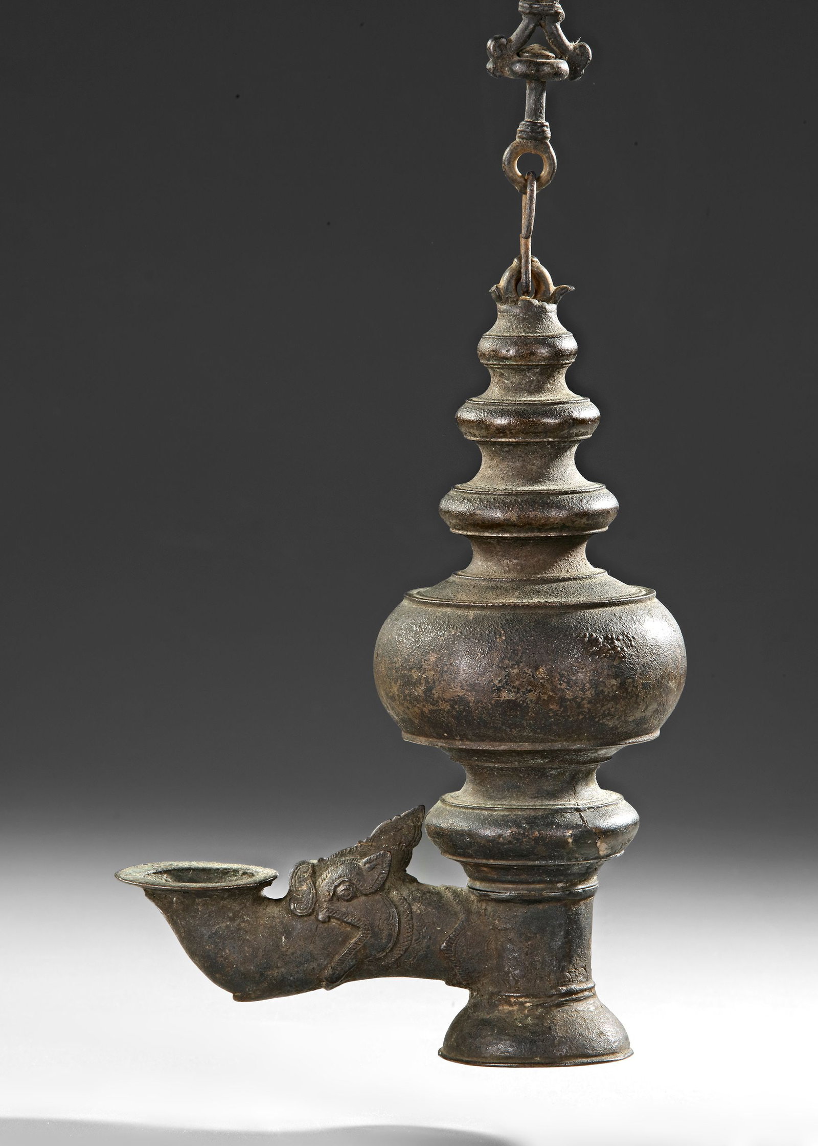 AN INDIAN TEMPLE BRONZE OIL LAMP, DECCAN OR SOUTH INDIA, 16TH-17TH CENTURY: The lamp is suspended by a chain with linked rings. The bulbous central body of the lamp would have held oil, its rounded form tapering elegantly above and below into ringed tiers. A horizontal spout 