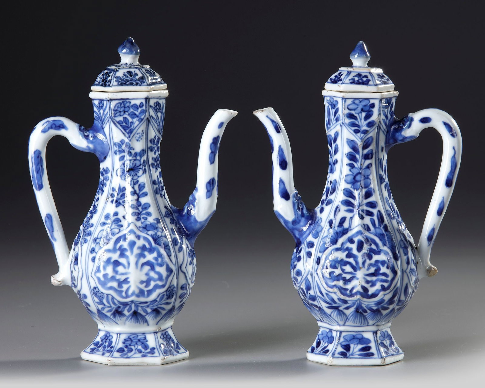 A PAIR OF CHINESE BLUE AND WHITE HEXAGONAL EWERS AND COVERS, KANGXI PERIOD (1662â€“1722): The ewers is modelled after a metalwork original for the Islamic market. The bodys is decorated with a c-shaped handle and s-shaped spout spewing from a mask-head, and each side is decorated with a te