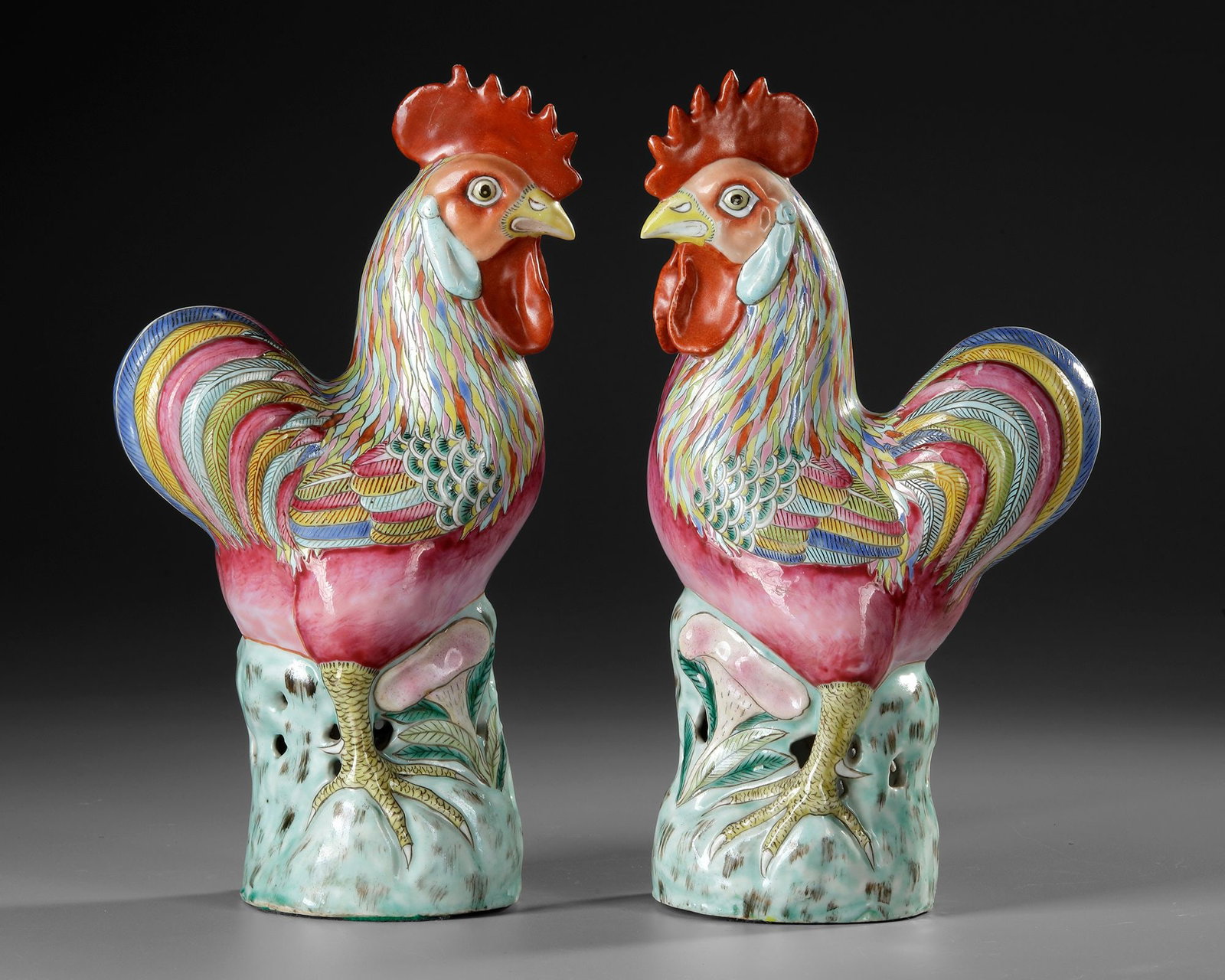 A PAIR OF CHINESE FAMILLE ROSE PORCELAIN ROOSTERS, 18TH CENTURY: A finely modelled Famille Rose porcelain pair of roosters, each naturalistically rendered standing upon a pierced, rockwork-form base. The birds are portrayed upright and alert, with elaborately model
