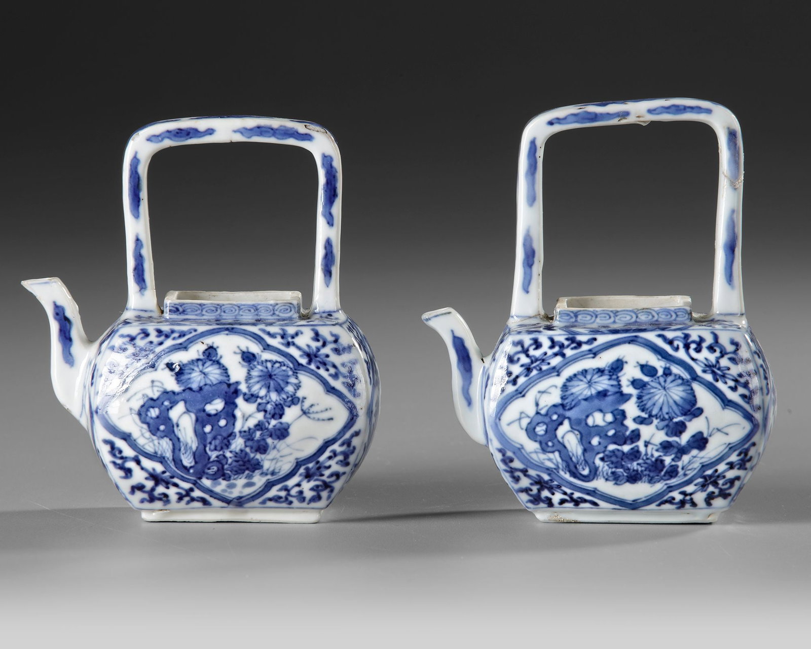 A PAIR OF CHINESE BLUE AND WHITE TEAPOTS WITHOUT LIDS, KANGXI PERIOD: A fine pair of Chinese blue-and-white porcelain teapots, each of compact, faceted form with gently rounded shoulders, short spreading foot and a tall, rectangular overhead handle. The vessels are fine