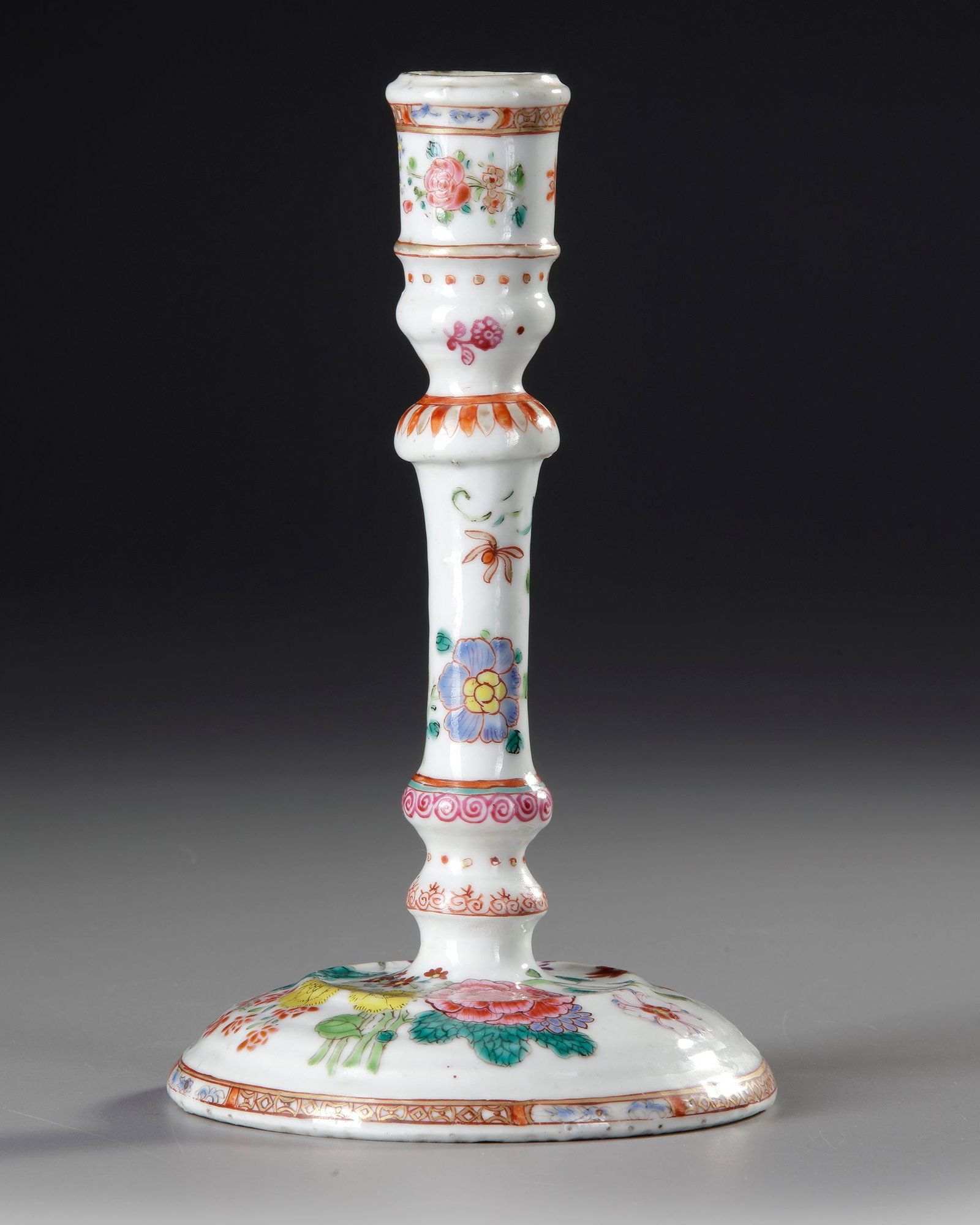 A CHINESE FAMILLE ROSE CANDLESTICK, 18TH CENTURY: Of slender baluster form, raised on a broad spreading circular foot, the stem with moulded knop and flared socket, finely decorated in famille rose enamels with flowering branches, chrysanthemum, peon