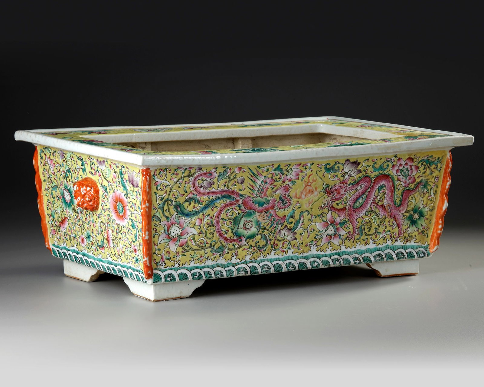 A CHINESE FAMILLE ROSE RECTANGULAR JARDINI??RE, 19TH CENTURY: Chinese porcelain jardini?¨re of rectangular form, finely decorated in the famille rose palette with sinuous dragons amidst flowering peonies, lotus and scrolling foliage, against a rich yellow groun