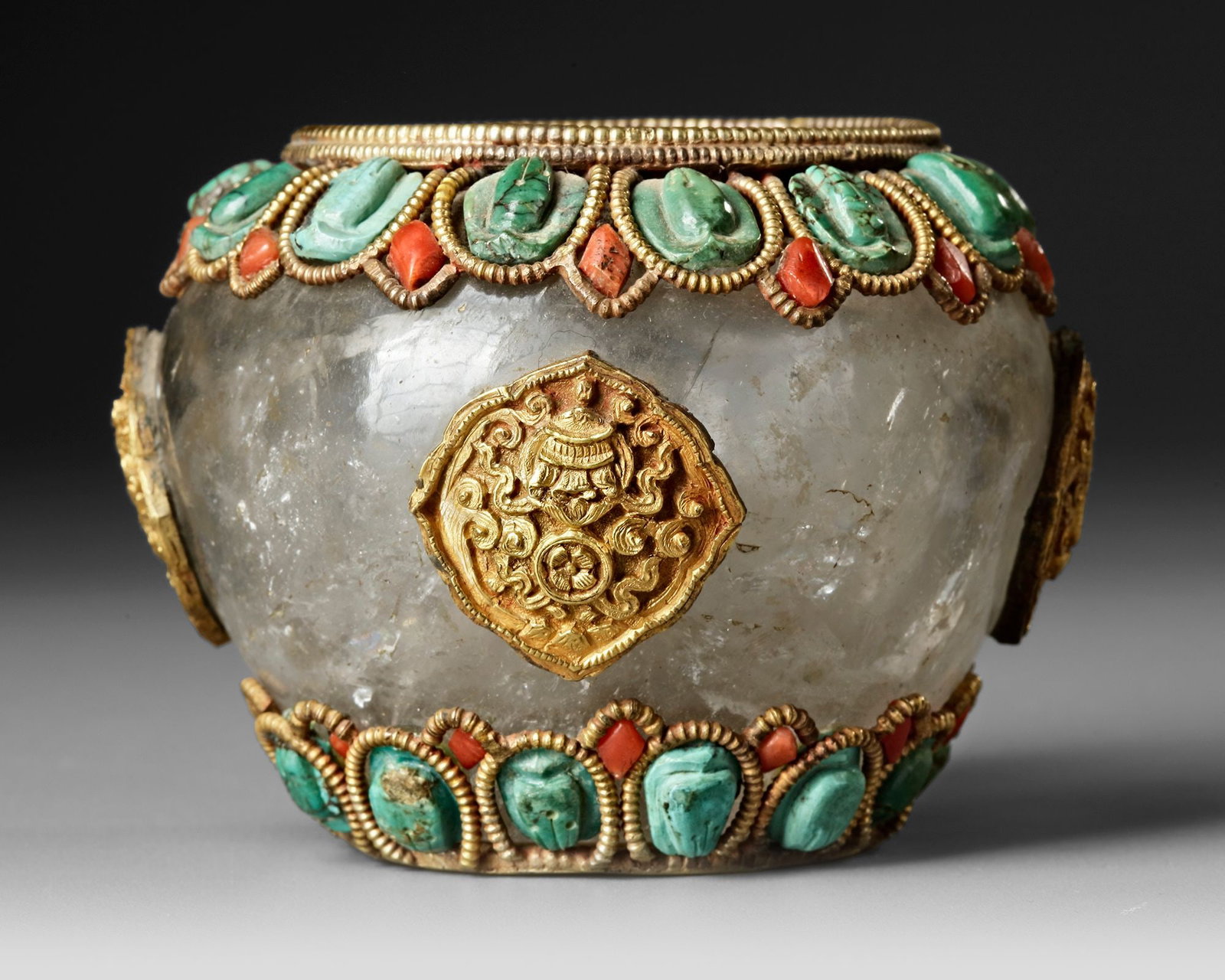 A TIBETAN ROCK CRYSTAL RITUAL POT, 19TH CENTURY: A rare Tibetan rock crystal ritual pot, finely mounted with gilt-metal ornaments and set with turquoise and coral cabochons. The translucent crystal body is embellished with traditional Himalayan deco
