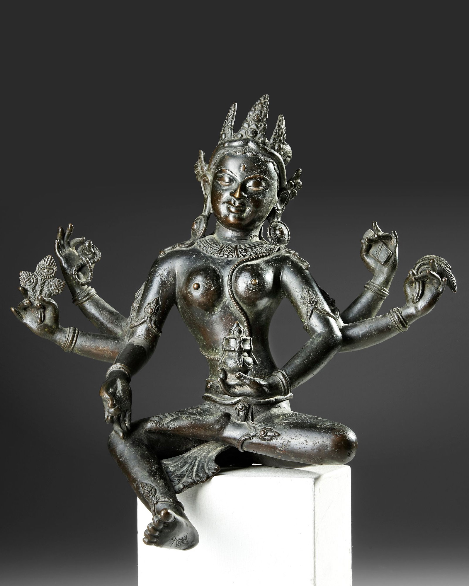A NEPALESE BRONZE FIGURE OF VASUDHARA, 17TH-18TH CENTURY: An elegant Nepalese bronze figure of Vasudhara, the Buddhist goddess of wealth, prosperity, and abundance. Seated in a graceful pose and depicted with multiple arms holding symbolic attributes, the sc