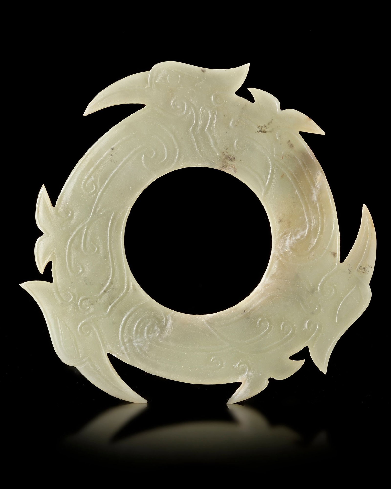 A LIGHT CELADON CHINESE JADE XUANJI, SHANG DYNASTY (c. 1600â€“1046 BC): A finely carved light celadon jade Xuanji disc from the Shang Dynasty, featuring elegant phoenix motifs and flowing scrollwork. The notched circular form symbolizes celestial harmony and ritual signif