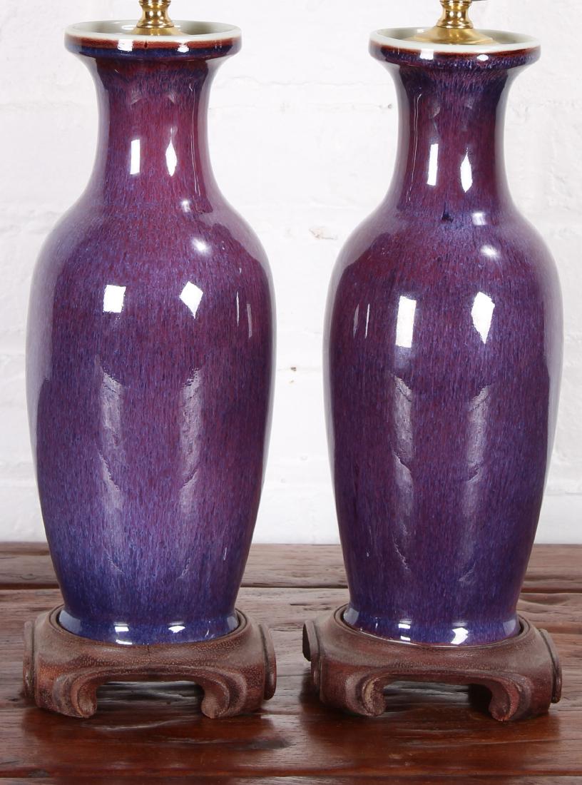 Pair of Asian/Chinese Purple Flambe Glazed Porcelain: A pair of Asian/Chinese purple flambe glazed porcelain lamps raided on wood bases. 20th century. Needs rewiring. Size: 16" H x 4" W