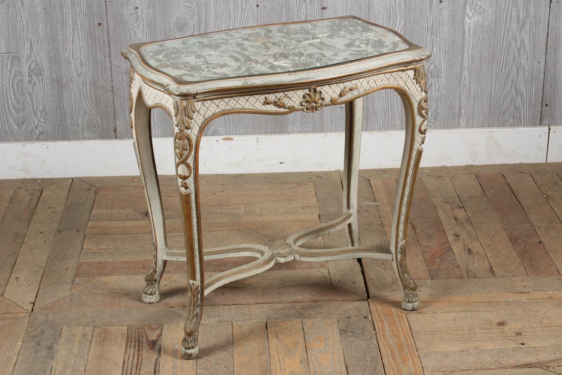Louis XV Gilt Painted Table w/ Embroidered Top: A French Louis XV style carved and panted side table with inset glass top with silver metallic fabric all supported on cabriole legs with shaped stretcher. Size: 24" H x 24" W x 15" D