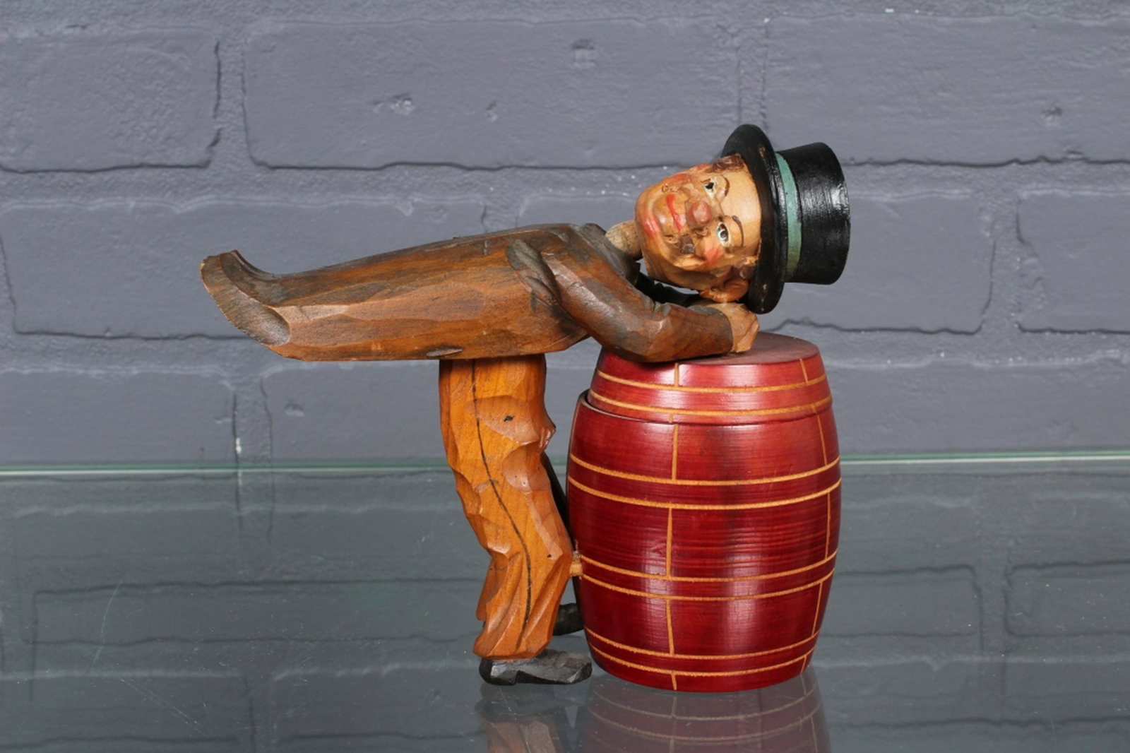 Anri Wood Carved Figural Cigarette Box: Anri Wood Carved Figural Cigarette Box, man leaning over top of barrel, when pressed on coat tail he opens the lid, head swivels, unmarked. Size: 6" H x 6.75" W x 2.5" D.