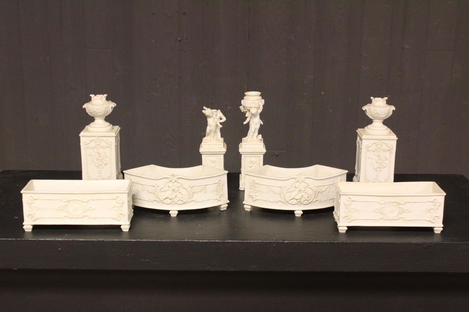 8 Piece Bisque Garniture Set: 8 Piece Bisque Garniture Set, decorated with cherubs, floral and foliate, urns, and blue underglaze mark Crown over V. Size: Largest: 7.5" H x 2.75" W x 2.75" D.