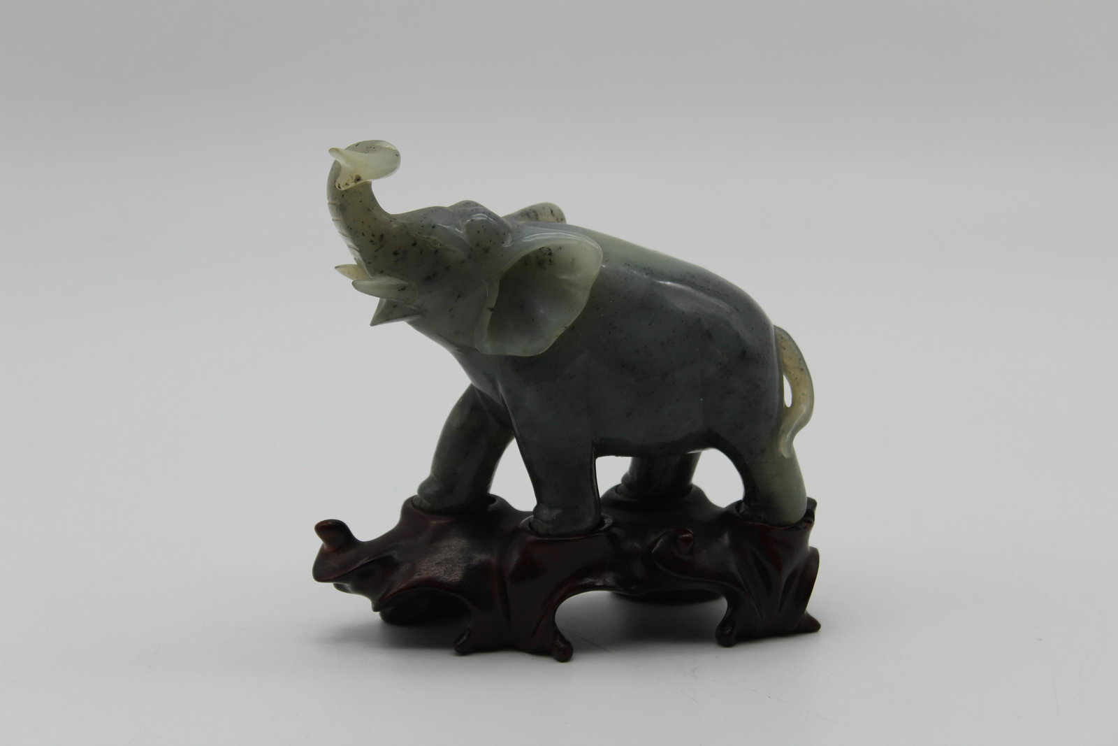 Carved Hardstone Elephant on Fitted Wooden Stand: Carved Hardstone Elephant on Fitted Wooden Stand, with raised trunk. Size: Elephant: 3.5" H x 5.5" W x 1.75" D.