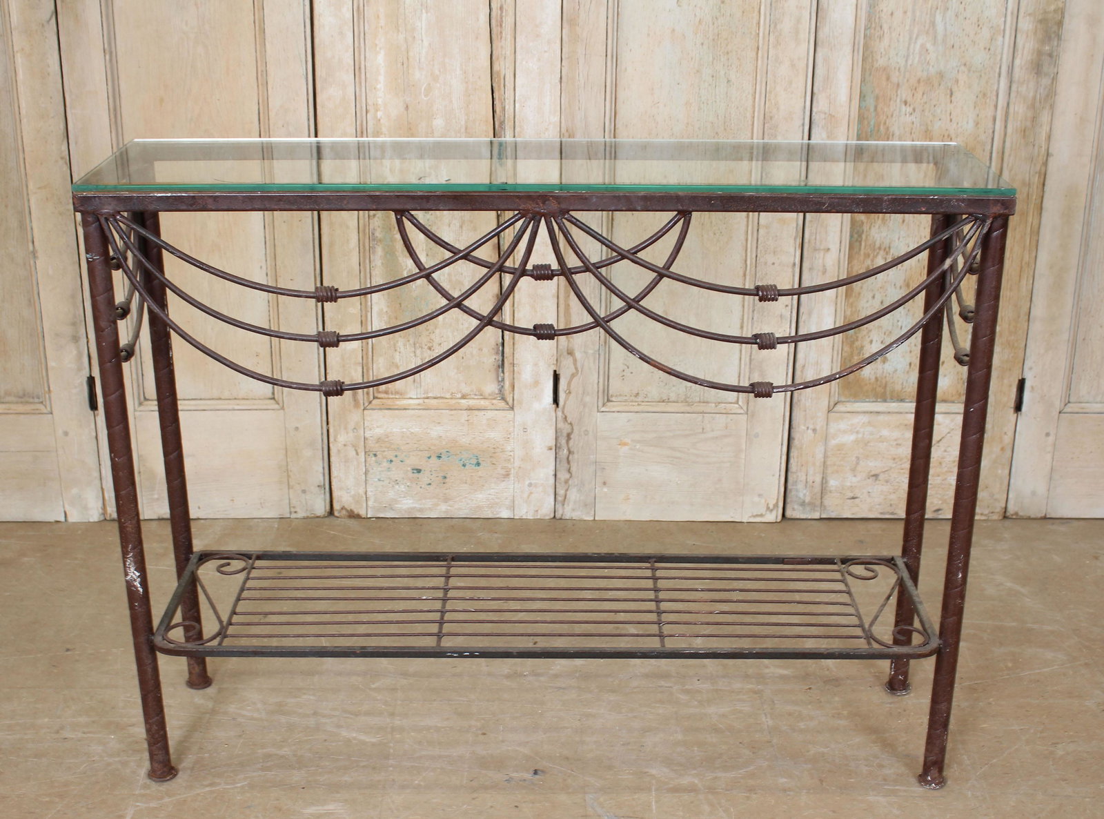 Glass Top Wrought Iron Consokle: A wrought iron console having glass top over decorated apron and lower shelf. 36" x 48" x 12"