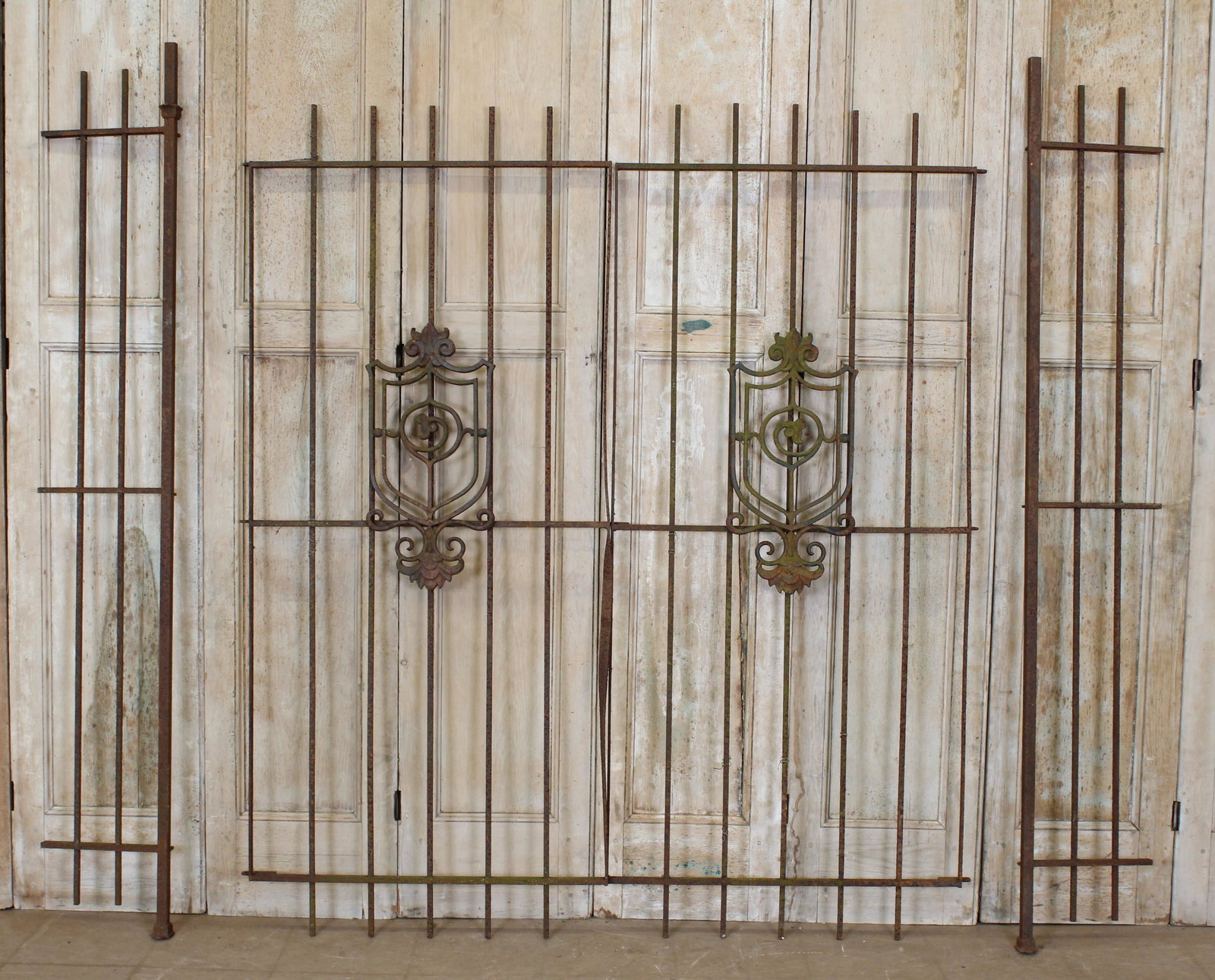 Cast and Wrought Iron Entry Gates: A pair of late 19th century cast iron and wrought iron entry estate gates, having central shield and scroll decoration. Size: 78"H x 34"W each panel Side panel 9"W