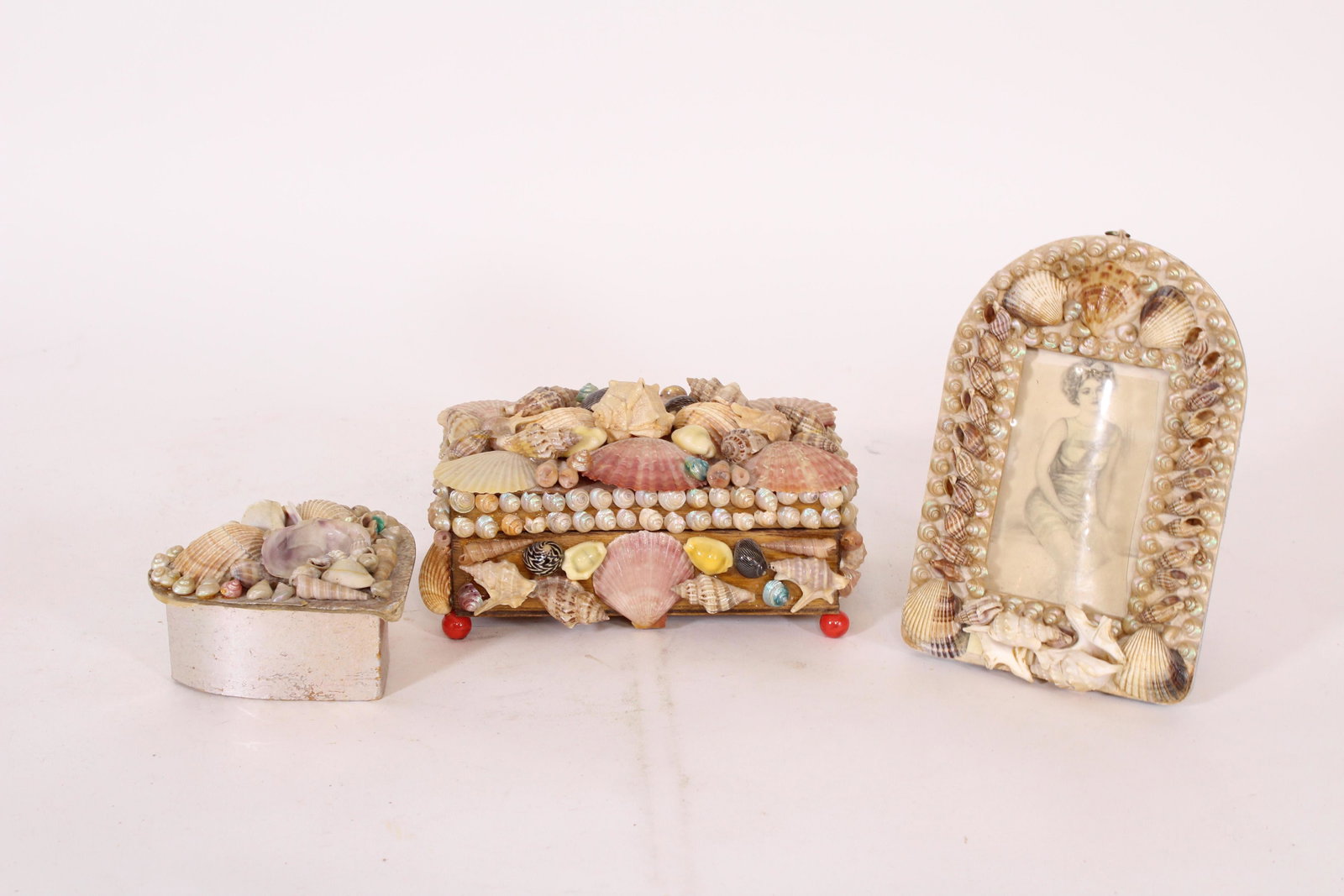 Three Piece Shell Decorated Dresser Lot: Three Piece Shell Decorated Dresser Lot, includes heat shaped box, rectangular box, and a picture frame. Size: Largest: 3" H x 7" W x 4.5" D. ***Please Note: This is an on-site online auction with spe