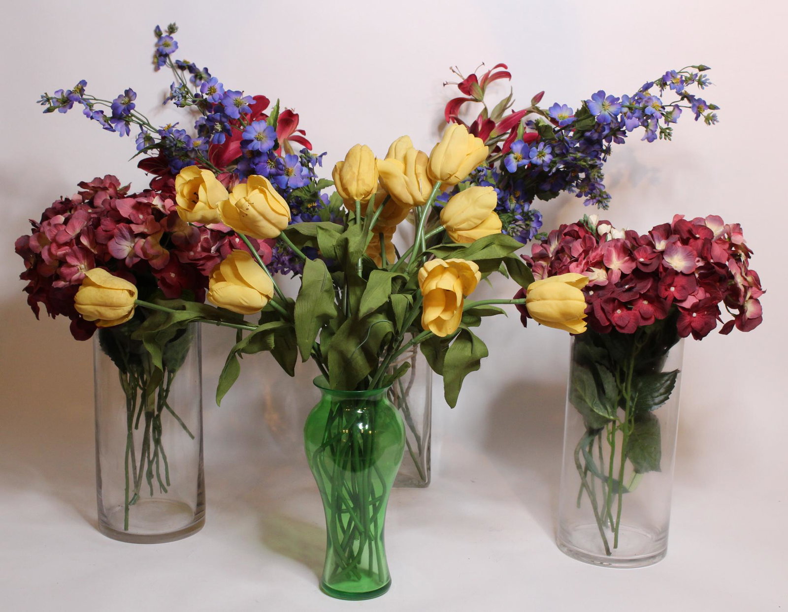 4 Large Glass Vases with Artificial Flowers: 4 Large Glass Vases with Artificial Floral arrangements, one vase green colored glass. Size: Largest: 14" H x 6" W x 6" D ***Please Note: This is an on-site online auction with specific Pick up terms 