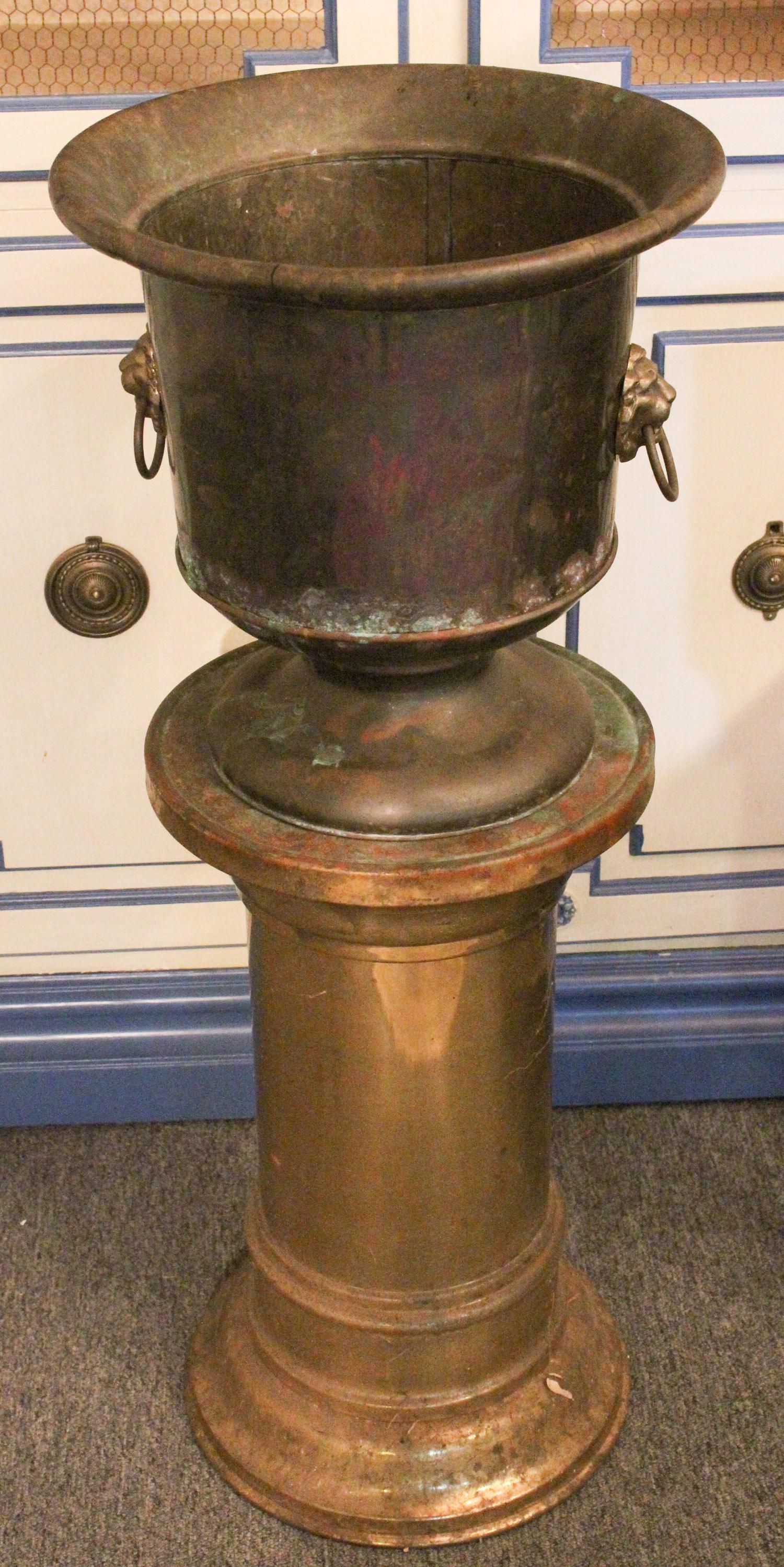 Brass Planter on Stand: Brass Planter on Stand. Urn form planter with lion head motif ring handles. Hallmarked Geo Ray, Buffalo, NY. With a brass plated pedestal stand. Size: pedestal 21" x 12.25" diameter, urn 14" high. ***