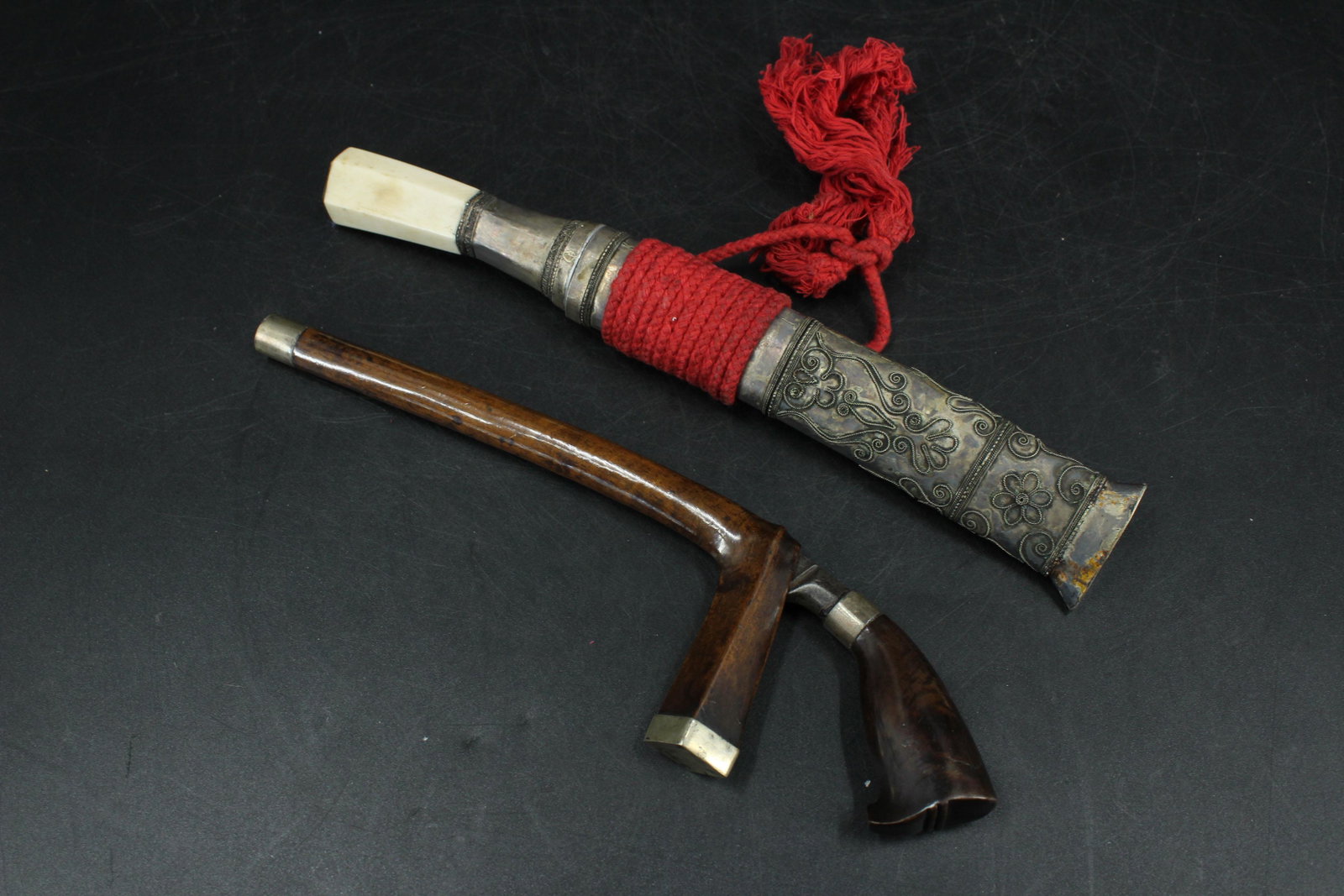 2 Ethnographic Daggers in Scabbards: 2 Daggers in Scabbards, includes a Ghurka Kukri dagger in metal scabbard with bone handle, and a Keris form dagger in a wood scabbard with silver plate mountings. Size: Largest: 10.5" H x 1.75" W x 1"
