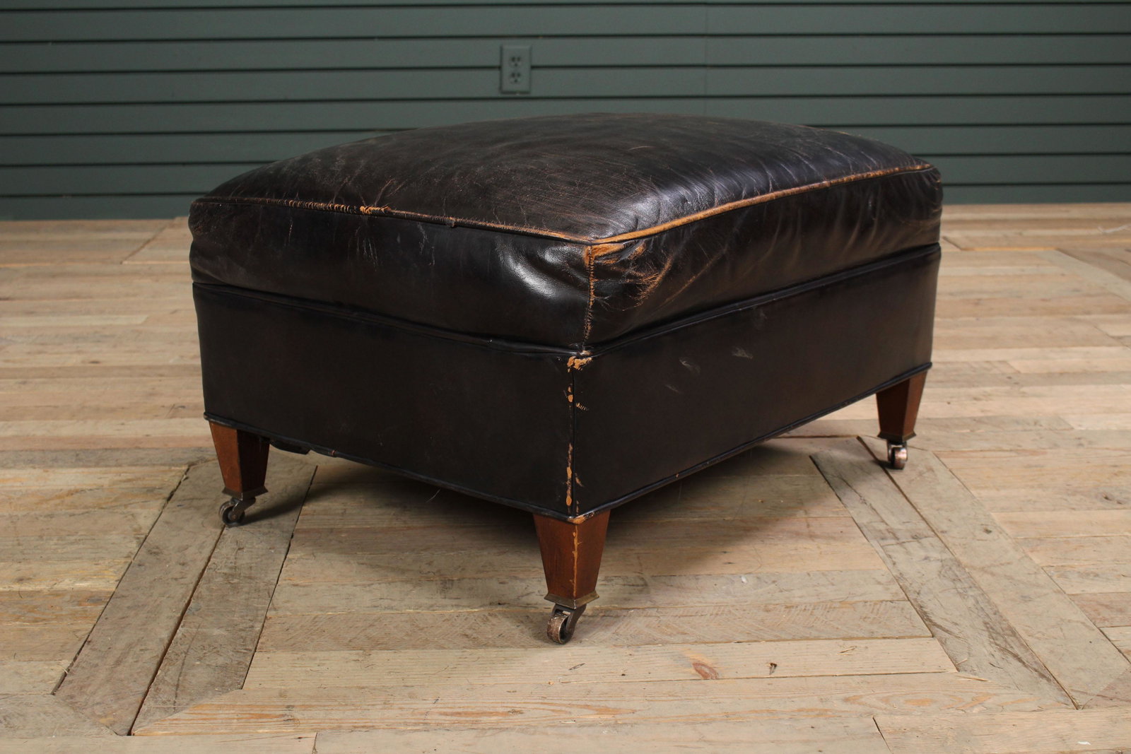 Vintage Mid C. Modern Leather Upholstered Ottoman: Vintage Mid C. Modern Leather Upholstered Ottoman having tapered legs with brass casters. Size: 15.5" H x 27.5" W x 20" D