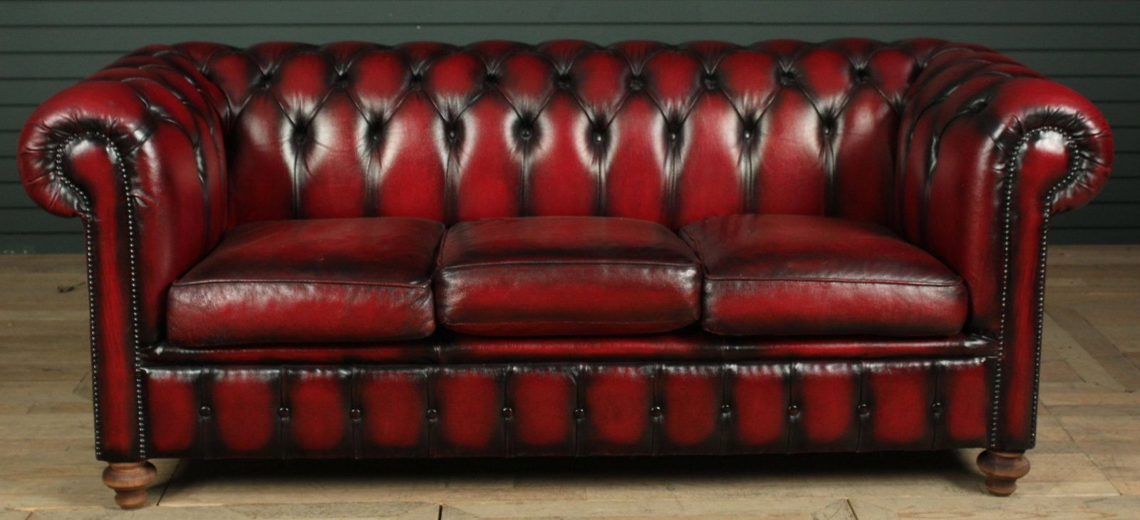 Leather Chesterfield: A classic leather Chesterfield having tufted back and rolled arms framing three loose cushions all raised on bun feet. Size: 31" H x 76" W x 33" D