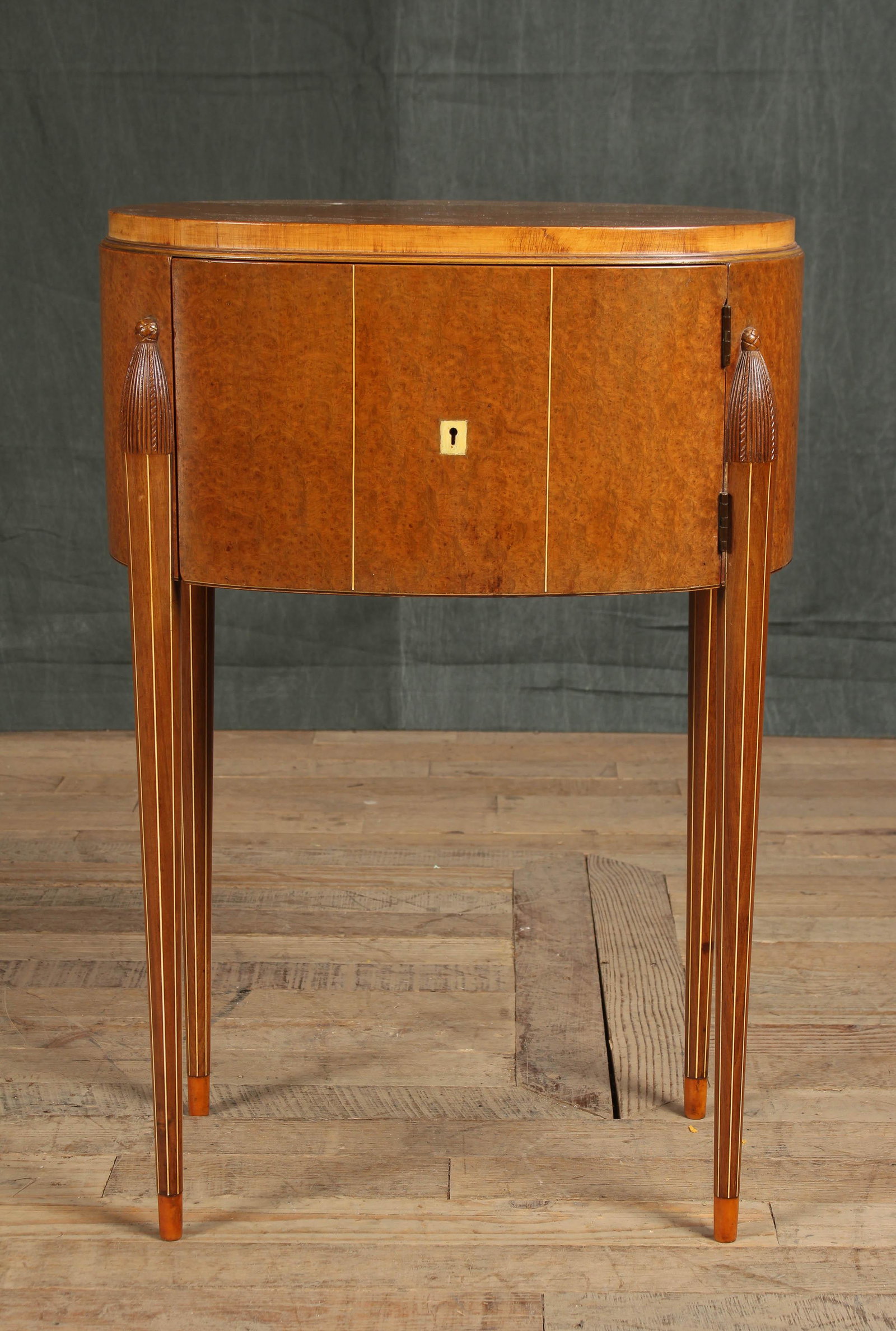 French Ruhlmann Style Side Cabinet: A very good Ruhlmann style burl and bone inlaid side cabinet having an oval top over single door with central escutcheon all supported on turned and tapered legs with line inlay. Size: 28"H x 19"W x 1