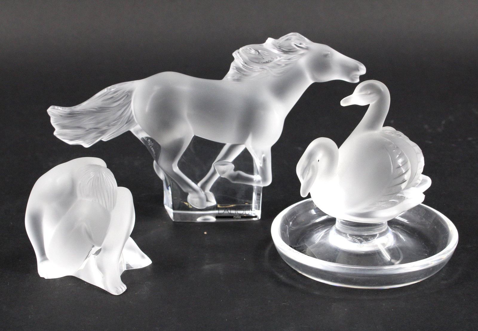 Lot of 3 Figural Lalique Bibelots: Lot of 3 Figural Lalique Bibelots. Size: 4.25"H x 7.5"W x 1.5"D Horse, 4"D x 4"D x 4"D Swans, and 2.75"H x 2.5"W x 2"D Figure