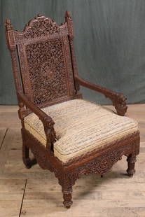 In the Manner of Lockwood De Forest: Exotic carved fantasy chair most likely Indian and in the style of Lockwood De Forest having extensive carved back panel framed by columns and open arms with stylized animal supports. Size: 42"H x 24"