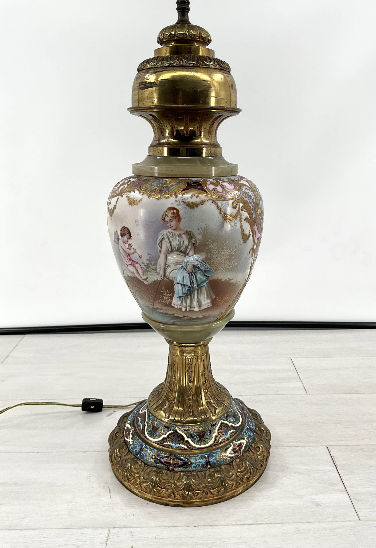 Gilt bronze lamp with painted scene of a maiden and cherub. Fits two bulbs, untested. Size:: Gilt bronze lamp with painted scene of a maiden and cherub. Fits two bulbs, untested. Size: Overall 39"H. 9" Dia. Base