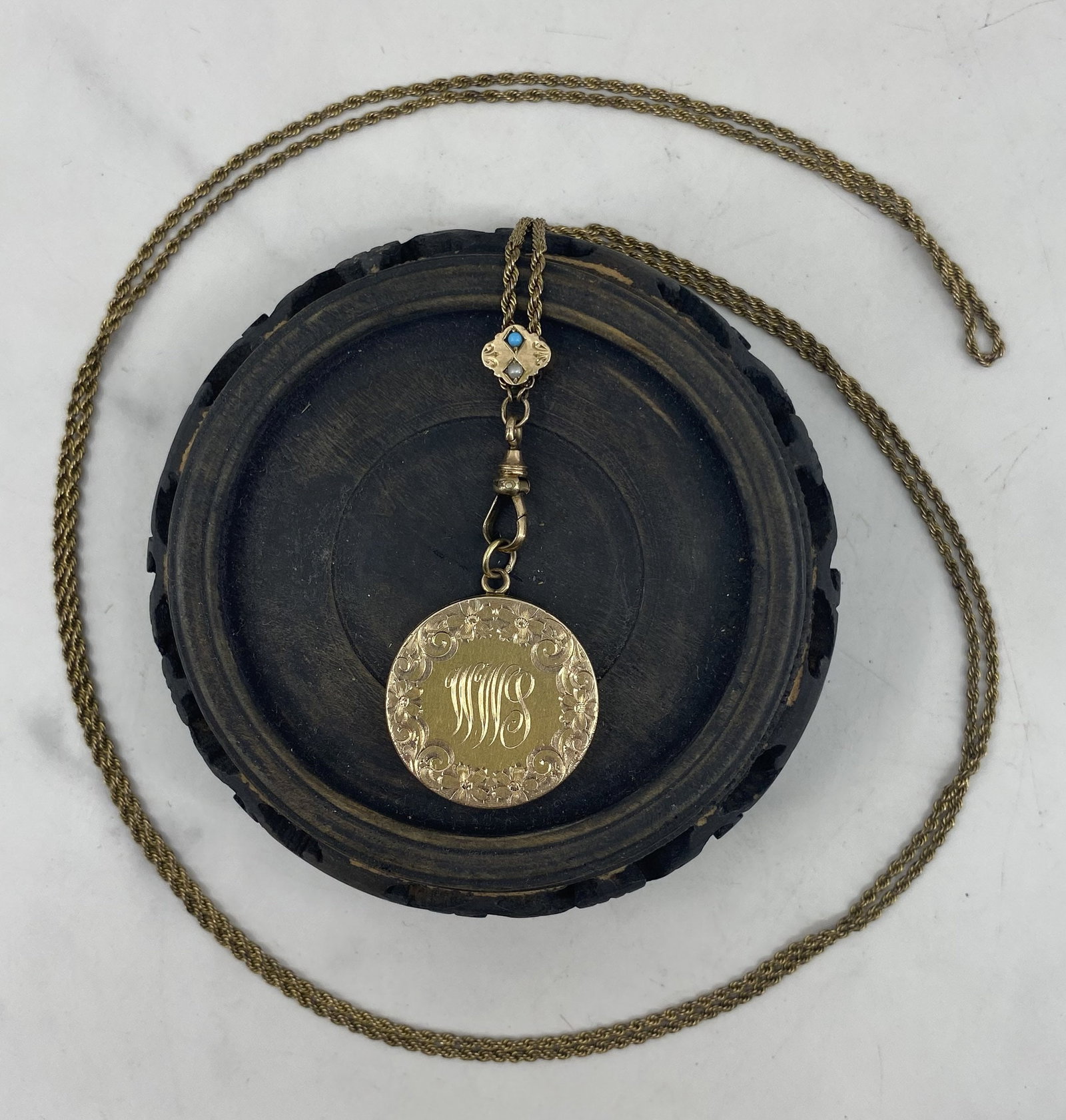 Gold Plate Locket on Gaurd Chain: Gold plate locket with floral motif and "WWS" monogram on a gold plate rope guard chain. Guard chain has a slide with a seed pearl and turquoise cabochon, dog clip is stamped "MS&S." Stand not include