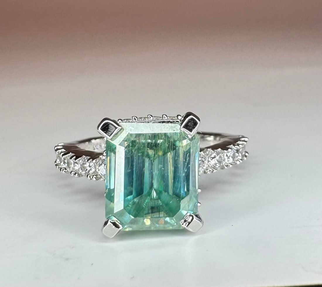 Sparkling 6.15 Ct Blue Ice Fire Moissanite Ring: This Ice Blue Fire Moissanite is a VVs1 6.15 Ct Emerald Cut. The Color is light sky greenish blue with a clarity of VVs1.Eye Clean Measuring 8.5 x 10.5 mm.. This Fire bursting out with a full spectrum