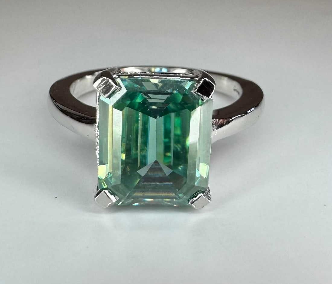 Dazzling 5.75 Ct Aqua Blue Fire Moissanite Ring: This Ice Blue Fire Moissanite is a VVs1 5.75 Ct Emerald Cut. The Color is a Vivid Greenish Blue Color and Is Eye Clean Measuring 9.5 x 11 mm.. This Fire Moissanite is bursting out with a full spectrum