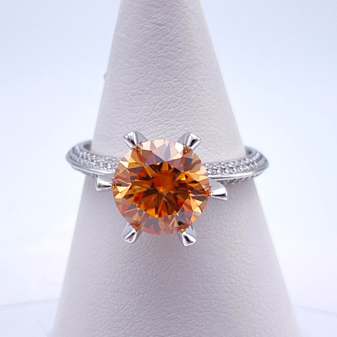 Plated 14KT White Gold 3 Ct VVs1 Orange Amber Fire Moissanite Ring: This Fine 3 Ct Moissanite Centerstone is a VVS1 Brilliant Round Cut Measuring 9 mm. The Color is a Striking Champagne Hue. This Fire Moissanite is near flawless and bursting out with a full spectrum