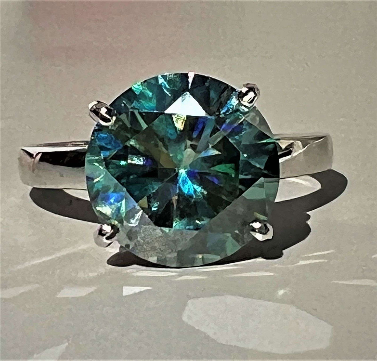 Plated 14KT White Gold 4.50ct Green Moissanite Ring: Dazzling 4.5 Ct Emerald Green Fire Moissanite Ring. This Rare Emerald Green Fire Moissanite is a VVs1 eye clean brilliant round cut measuring approx. 10.3 mm.It is mounted in .925 solid sterling silve