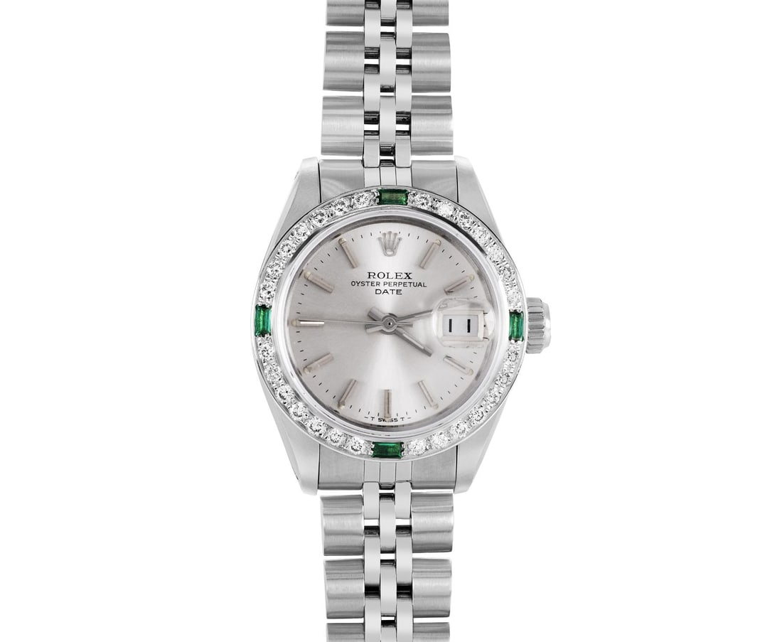 Rolex Ladies Stainless Steel Emerald And Diamond Bezel Date Watch: This Lady Rolex Date watch features a silver dial with index hour markers and a custom sapphire crystal, with a magnified date window. The timepiece has custom 18K white gold diamond and emerald bezel