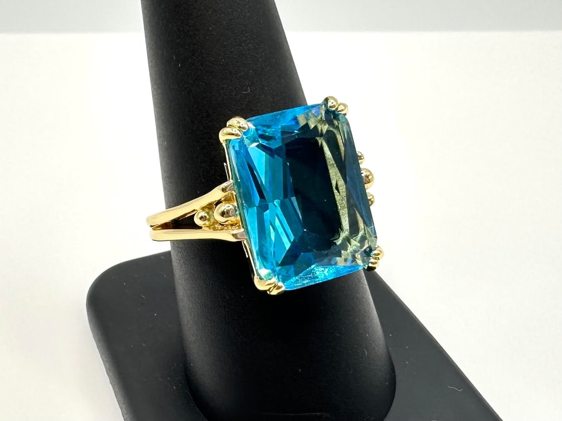 Breathtaking 14 kt Yellow Gold Plate 6.5 Ct Emerald Cut Simulated Swiss Blue Topaz Ring: Breathtaking 14 kt Yellow Gold Plate 6.5 Ct Emerald Cut Simulated Swiss Blue Topaz Ring. This Swiss Blue Topaz is Center-Stone is an Eye-Clean Emerald Cut measuring 10 x 12 mm. It is mounted in elabor