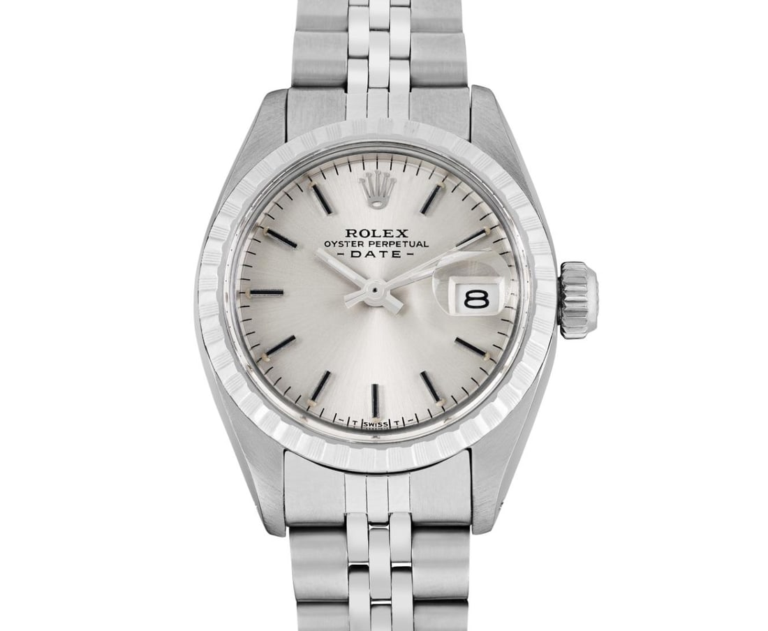 Rolex Ladies 26MM Date Wristwatch: This Lady Rolex Date watch features a silver dial with index hour markers and a custom plastic crystal, with a magnified date window. The timepiece has Rolex stainless steel engine turn bezel. The Rol