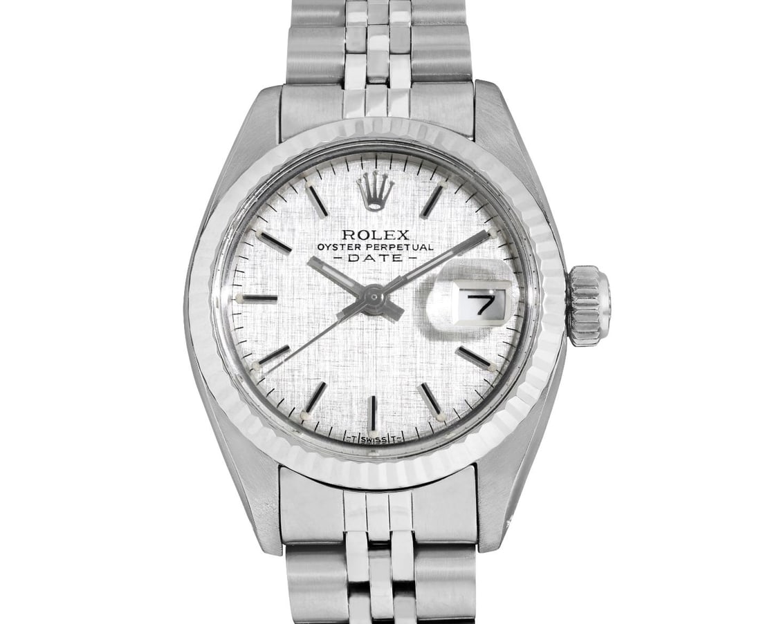 Rolex Ladies Stainless Steel 14K Fluted Bezel Date Watch: This Lady Rolex Date watch features a silver linen dial with index hour markers and a custom plastic crystal, with a magnified date window. The timepiece has Rolex 14K white gold fluted bezel. The Rol