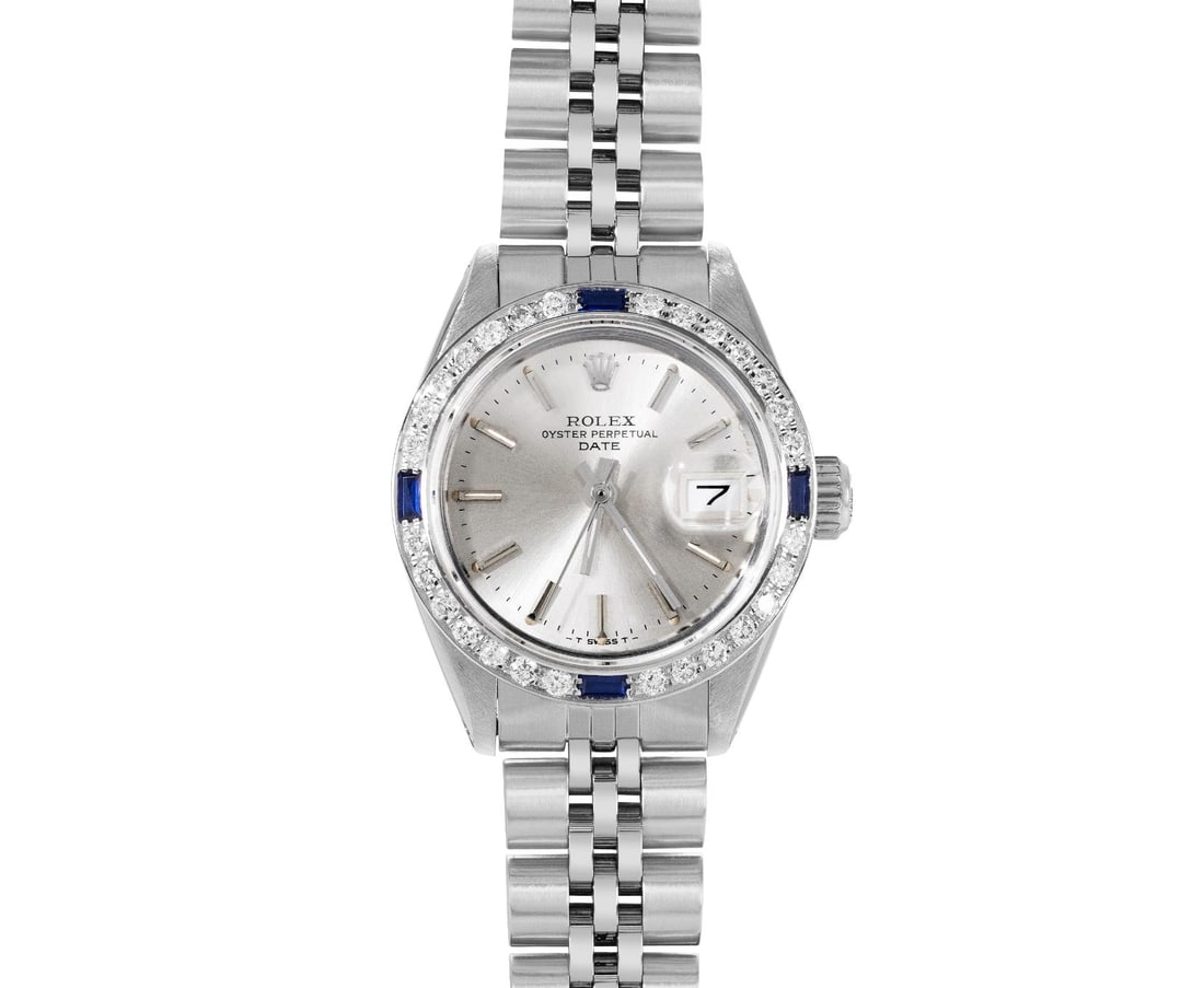 Rolex Ladies Stainless Steel Sapphire And Diamond Bezel Date Watch: This Lady Rolex Date watch features a silver dial with index hour markers and a custom sapphire crystal, with a magnified date window. The timepiece has custom 18K white gold diamond and sapphire beze