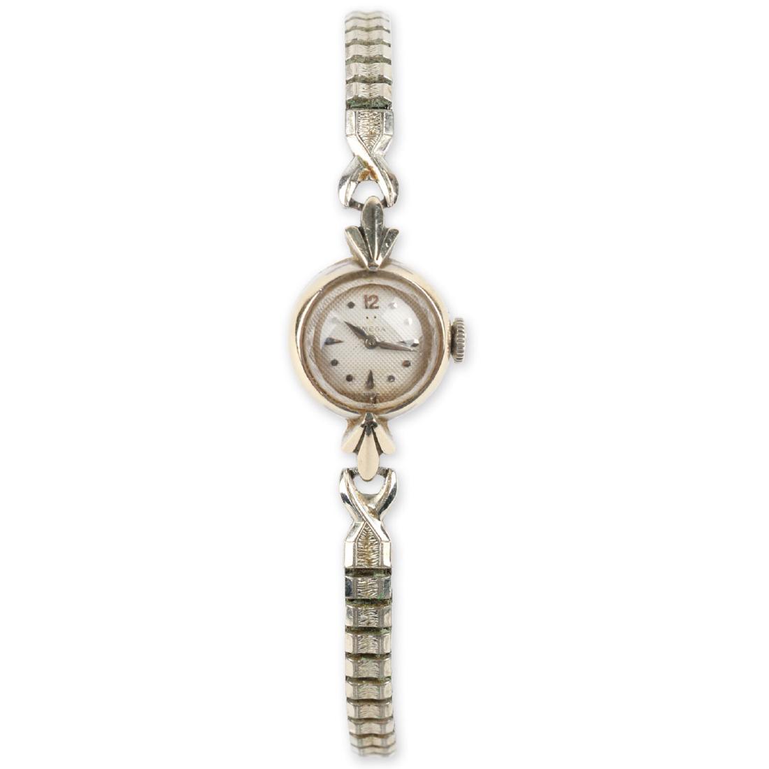 Ladies 14K White Gold Omega Cocktail Wristwatch: 14K white gold case. Textured white dial with white gold hour markers. Gold filled stretch band. Omega crown. Manual winding movement. CONDITION: Excellent with light scratches to the beveled glass cr