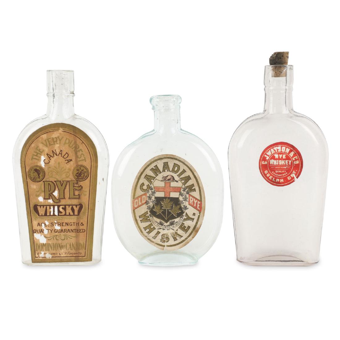 Three Labelled Early Glass Whiskey Bottles: All three with flattened side profiles, 6.5 to 8" high: intact paper labels - 'C.J. Watson & Co., Rye Whiskey Guelph, Ont.' ; 'Rye Whisky Dominion of Canada, R.H. Howard & Co., Toronto; Old Rye Canadi