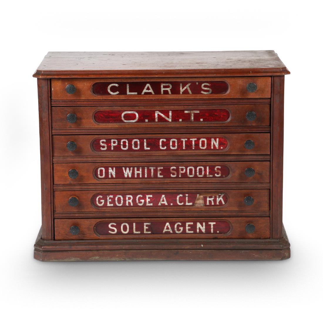Clark's Spool Cabinet: American. Cranberry glass advertising panels cut to clear. Clark's. 29" x 18.5" x 22". Three glass advertising panels are broken. Replacement hardware.