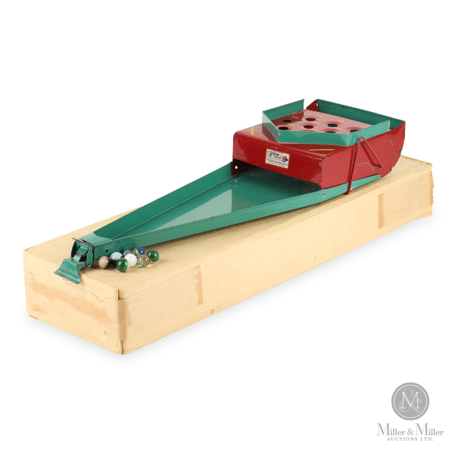 Hand Toys Canada Marble Flicking Game: Canadian. 1950. Pressed steel. A marble flicking game with box and marbles. Made in Canada by Hand Toys. T.W. Hand Fireworks co Ltd. Cooksville, Ontario. Comes with box and marbles. 3"H x 21"L x 6"W.