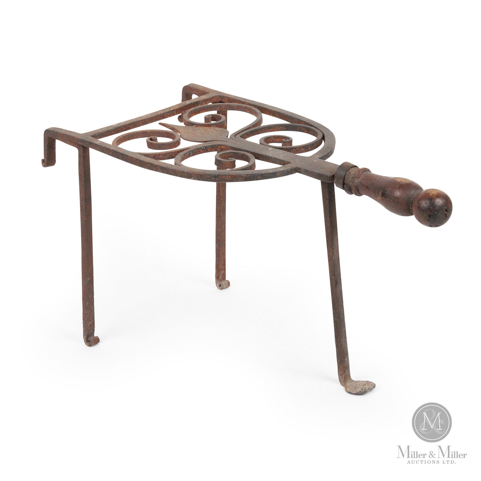 Hand Forged Fireplace Trivet: A standing trivet on three legs, one with a penny foot and the other two having a curled toe. With the original turned wooden handle, the platform has a hand-forged spear tip surrounded by four ram's