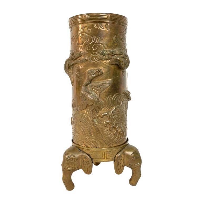 Heavy Vintage Chinese Brass Cranes Cylinder Vase: A vintage Chinese heavy gilt brass cylinder footed hat vase having raised cranes amongst clouds flying over crashing waves design with figural tripod elephant head feet. Bottom with impressed six char