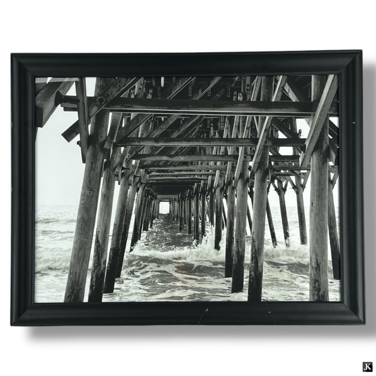 Black & White Photo Print "Under The Pier": Black & White Photo Print "Under The Pier". Unsigned. Framed and under glass. Some wear to frame or in good condition. Measures 21-1/4" x 27-1/4" overall including frame. LA/B13/SH:18B